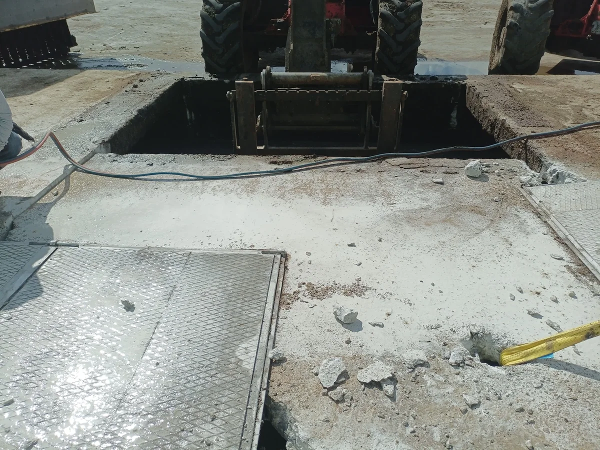 Ağır saha makinesi yanında açılmış beton döşeme ve derin boşluk.