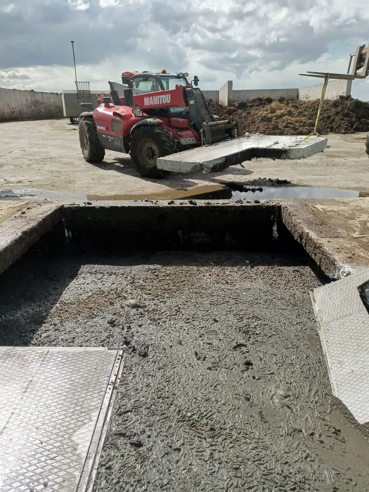 Açılmış döşeme boşluğu, kırılmış beton kenarları ve saha makinesi.